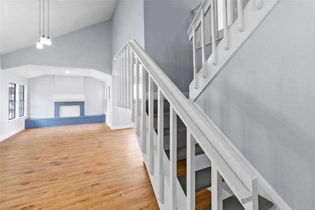 staircase with a fireplace, hardwood / wood-style flooring, and high vaulted ceiling