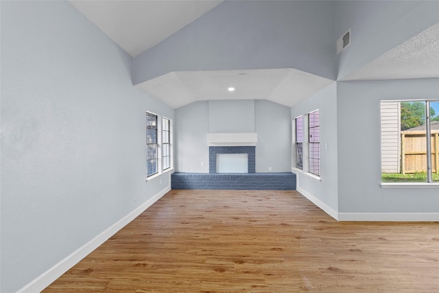 unfurnished living room featuring a fireplace, a textured ceiling, light wood-type flooring, and vaulted ceiling