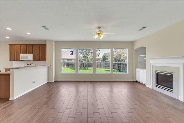 unfurnished living room featuring a tiled fireplace, ceiling fan, and built in features