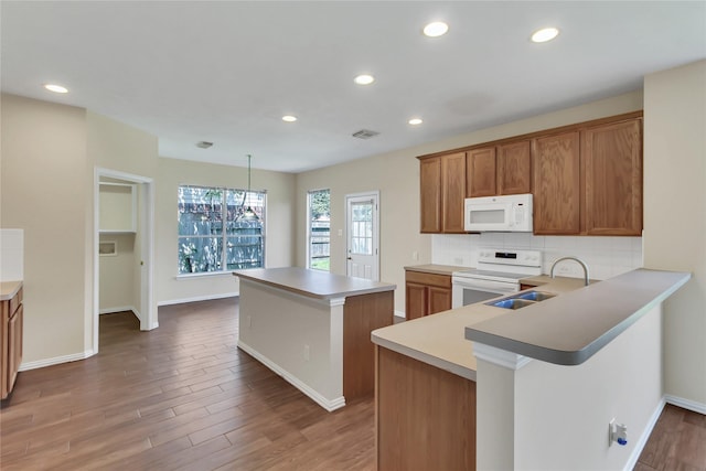 kitchen with sink, kitchen peninsula, pendant lighting, white appliances, and a kitchen island