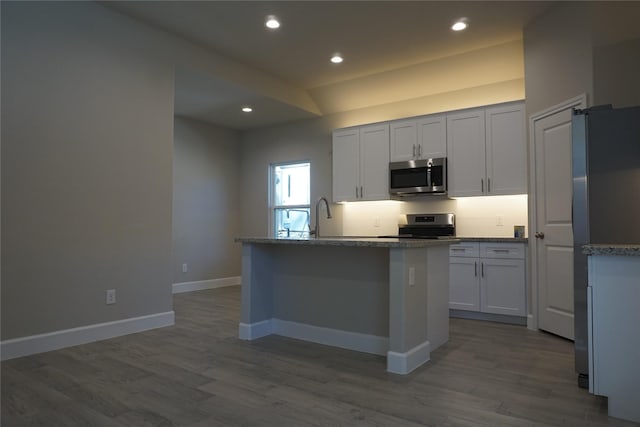 kitchen featuring a center island with sink, white cabinets, light stone countertops, wood-type flooring, and stainless steel appliances