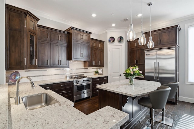 kitchen with light stone counters, high end appliances, decorative light fixtures, a kitchen bar, and sink