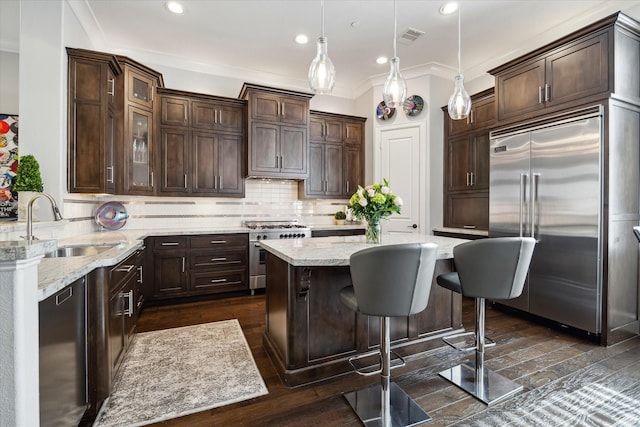 kitchen with sink, decorative light fixtures, dark brown cabinetry, high quality appliances, and dark wood-type flooring