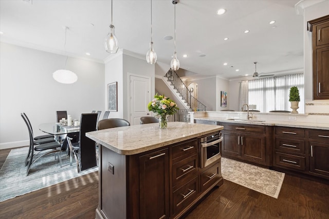 kitchen featuring hanging light fixtures, ceiling fan, dark wood-type flooring, a kitchen island, and sink