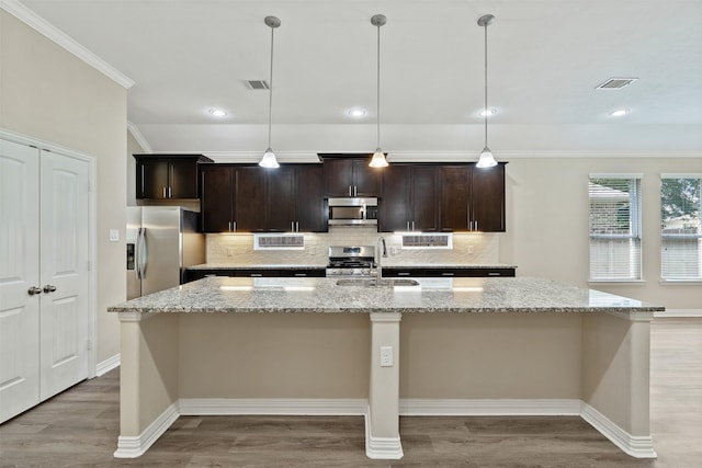 kitchen featuring decorative light fixtures, stainless steel appliances, a center island with sink, and sink