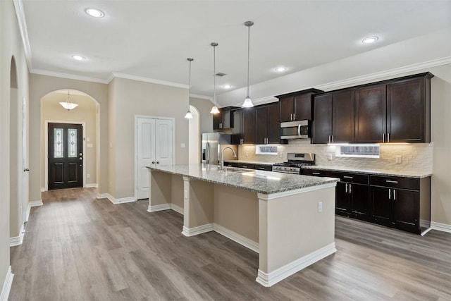 kitchen with appliances with stainless steel finishes, light stone counters, a kitchen island with sink, sink, and hanging light fixtures