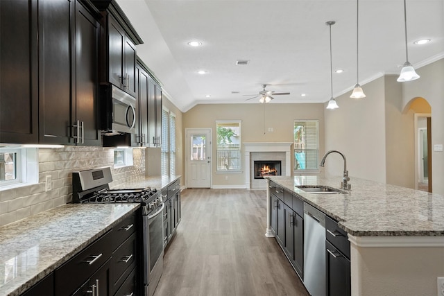 kitchen featuring stainless steel appliances, a kitchen island with sink, ceiling fan, sink, and decorative light fixtures