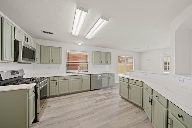 kitchen with kitchen peninsula, green cabinets, plenty of natural light, appliances with stainless steel finishes, and sink