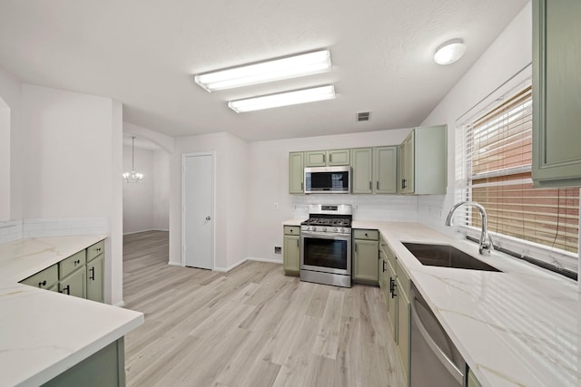 kitchen featuring stainless steel appliances, green cabinetry, sink, an inviting chandelier, and light stone countertops