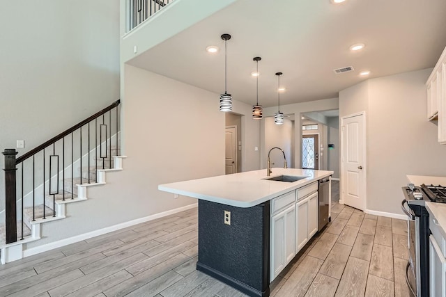 kitchen featuring sink, stainless steel appliances, an island with sink, decorative light fixtures, and white cabinets