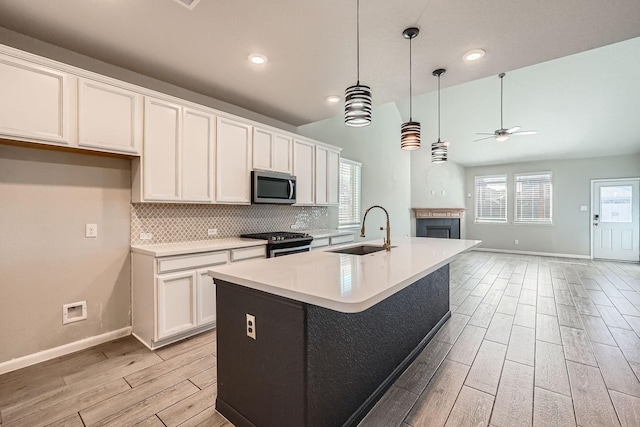 kitchen with stainless steel appliances, ceiling fan, sink, white cabinets, and an island with sink