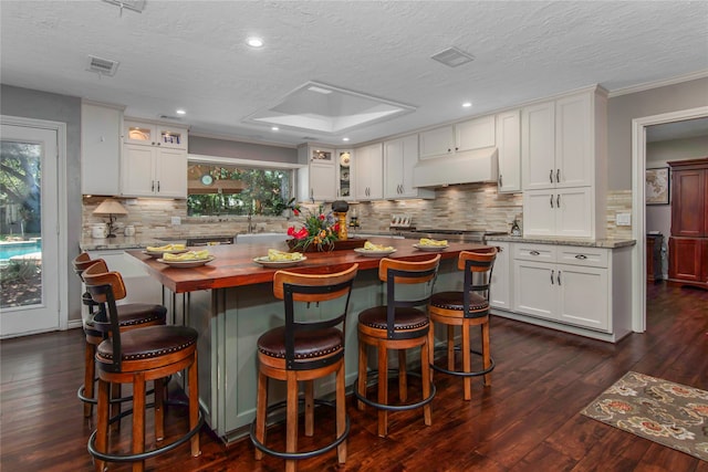 kitchen with light stone countertops, a breakfast bar, white cabinets, and custom exhaust hood