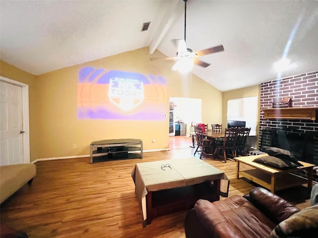 living room featuring lofted ceiling with beams, hardwood / wood-style flooring, a brick fireplace, and ceiling fan