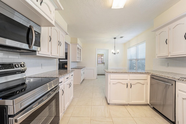 kitchen with pendant lighting, light tile patterned floors, appliances with stainless steel finishes, white cabinetry, and a chandelier