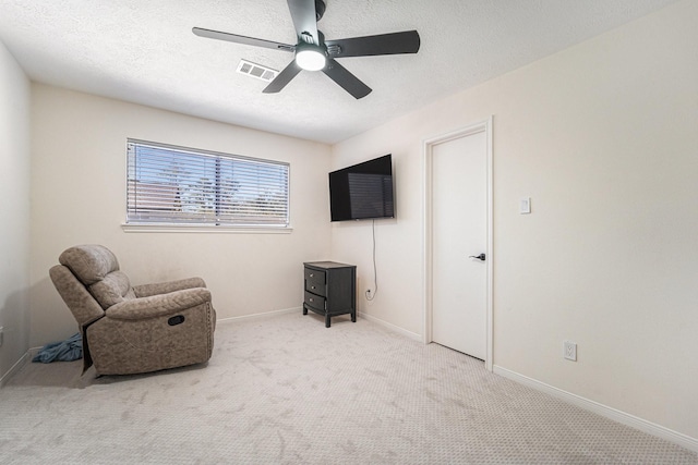 living area with a textured ceiling, light colored carpet, and ceiling fan