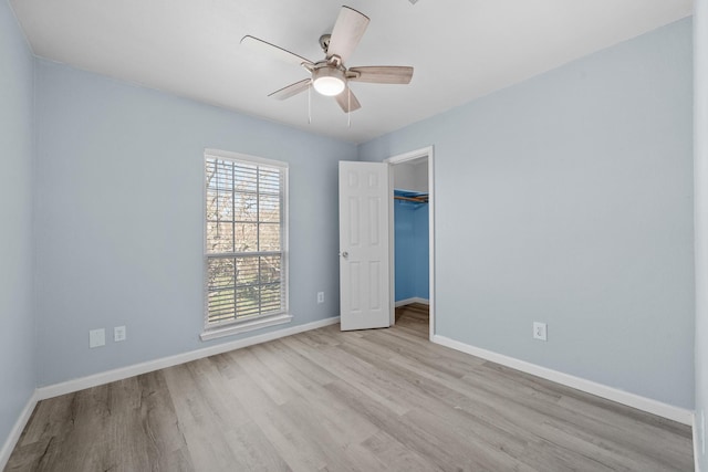 unfurnished bedroom featuring a spacious closet, a closet, light hardwood / wood-style flooring, and ceiling fan