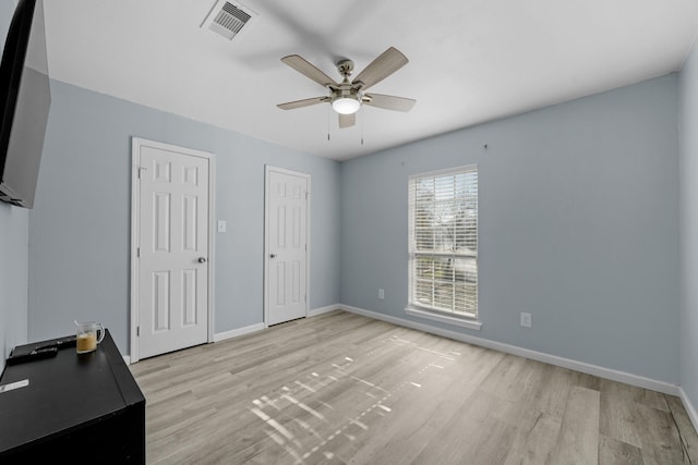 unfurnished bedroom with ceiling fan, light hardwood / wood-style floors, and two closets