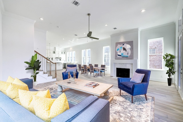 living room with light hardwood / wood-style floors, ceiling fan, crown molding, and a premium fireplace