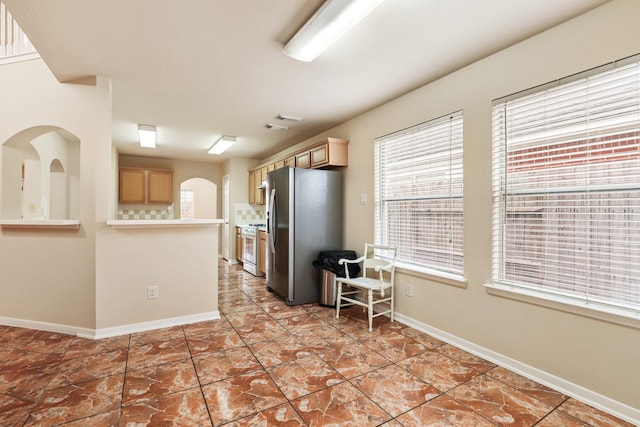 kitchen with light tile patterned flooring, stainless steel refrigerator, light brown cabinetry, and white gas range