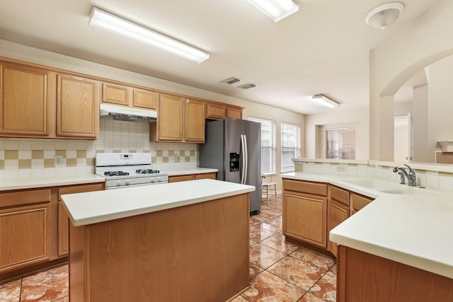 kitchen featuring kitchen peninsula, stainless steel fridge, sink, white gas range, and tasteful backsplash