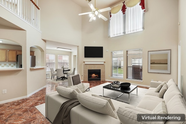 living room featuring ceiling fan, a tiled fireplace, and a towering ceiling