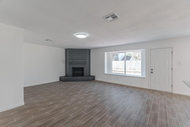 unfurnished living room featuring a textured ceiling, hardwood / wood-style flooring, and a brick fireplace