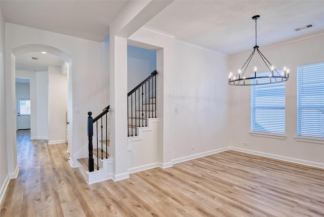 unfurnished dining area with light wood-type flooring, ornamental molding, and an inviting chandelier