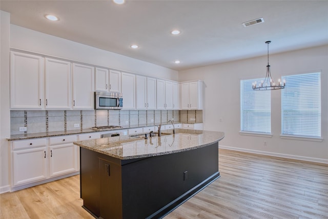 kitchen with appliances with stainless steel finishes, sink, pendant lighting, white cabinets, and an island with sink