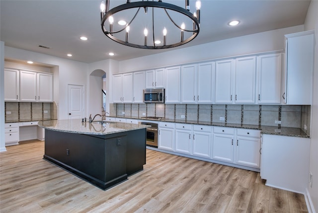 kitchen with white cabinets, pendant lighting, stainless steel appliances, and a center island with sink