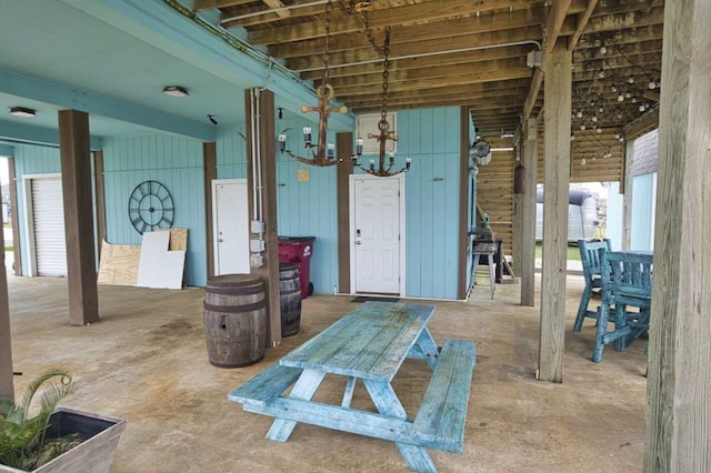 miscellaneous room with concrete flooring, a notable chandelier, and wood walls