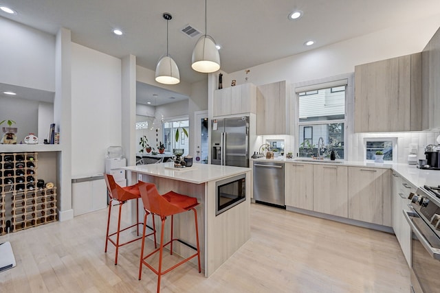 kitchen featuring sink, hanging light fixtures, stainless steel appliances, light hardwood / wood-style floors, and a kitchen island