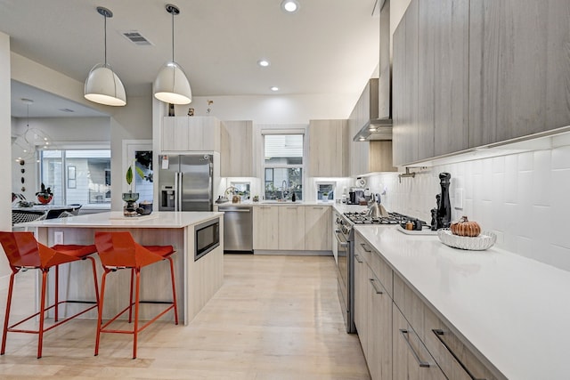 kitchen with light brown cabinetry, backsplash, a breakfast bar, stainless steel appliances, and hanging light fixtures