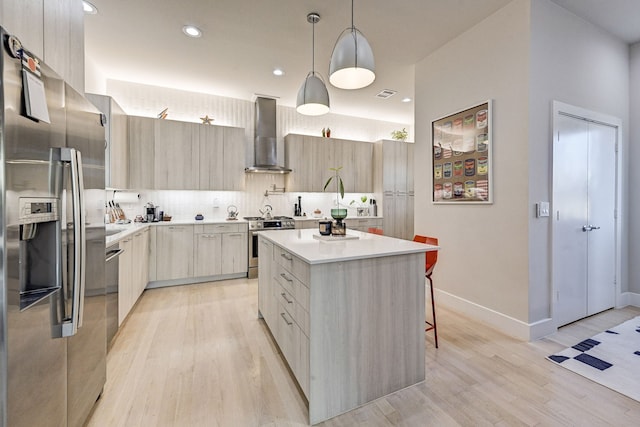 kitchen with appliances with stainless steel finishes, a breakfast bar, wall chimney range hood, pendant lighting, and a center island