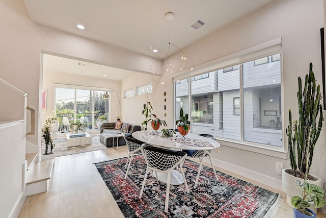 dining space with light hardwood / wood-style floors, plenty of natural light, and a notable chandelier