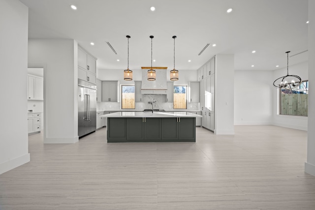 kitchen featuring decorative light fixtures, a notable chandelier, a kitchen island with sink, and built in fridge