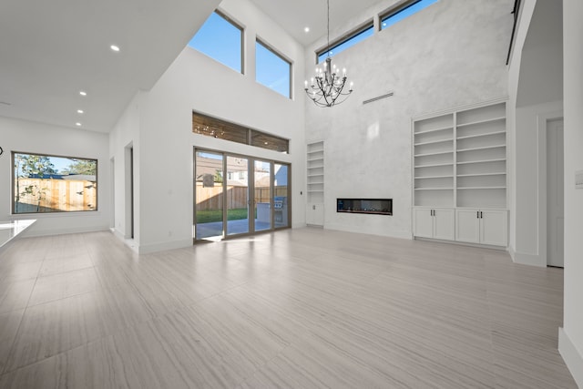 unfurnished living room featuring a high ceiling, a chandelier, and built in shelves