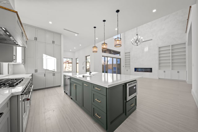 kitchen with stainless steel appliances, sink, decorative light fixtures, range hood, and a center island with sink