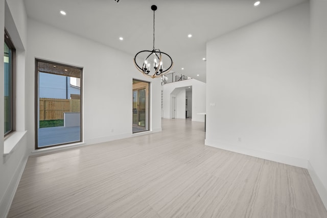 unfurnished living room featuring an inviting chandelier and light hardwood / wood-style floors