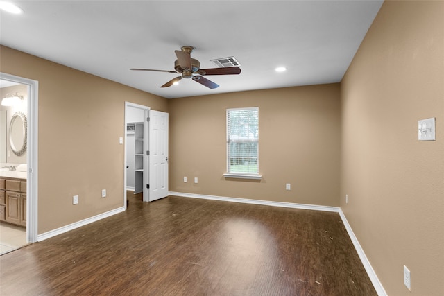 unfurnished bedroom featuring dark wood-type flooring, a walk in closet, ceiling fan, connected bathroom, and a closet