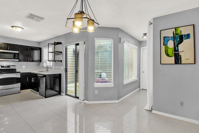 kitchen with a textured ceiling, decorative light fixtures, light tile patterned floors, and stainless steel appliances