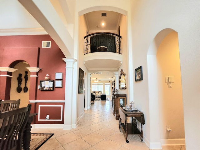 hallway featuring light tile patterned flooring, ornate columns, ornamental molding, and a towering ceiling