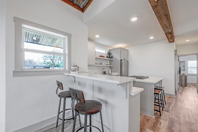 kitchen with a kitchen breakfast bar, kitchen peninsula, stainless steel fridge, beam ceiling, and white cabinetry