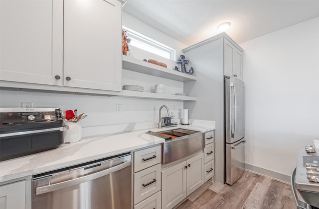 kitchen featuring appliances with stainless steel finishes, light wood-type flooring, light stone counters, sink, and white cabinets