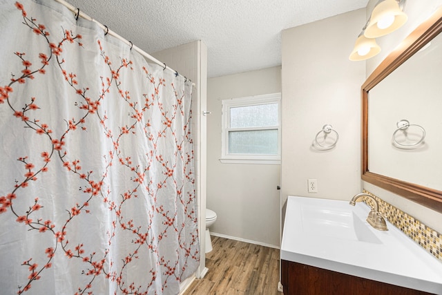 bathroom featuring wood-type flooring, vanity, walk in shower, toilet, and a textured ceiling