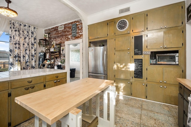 kitchen featuring wooden counters, stainless steel refrigerator, ornamental molding, and brick wall