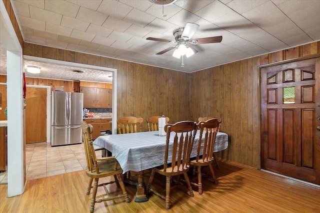 dining space with ceiling fan, light wood-type flooring, and wooden walls