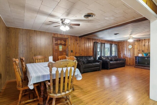 dining room featuring light hardwood / wood-style flooring, ceiling fan, and wooden walls