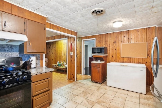 kitchen featuring light tile patterned floors, stainless steel appliances, crown molding, and wooden walls