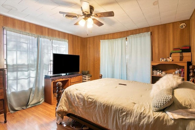 bedroom featuring ceiling fan, light hardwood / wood-style flooring, and wood walls