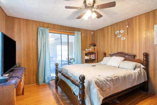 bedroom with access to outside, ceiling fan, light hardwood / wood-style floors, and wood walls